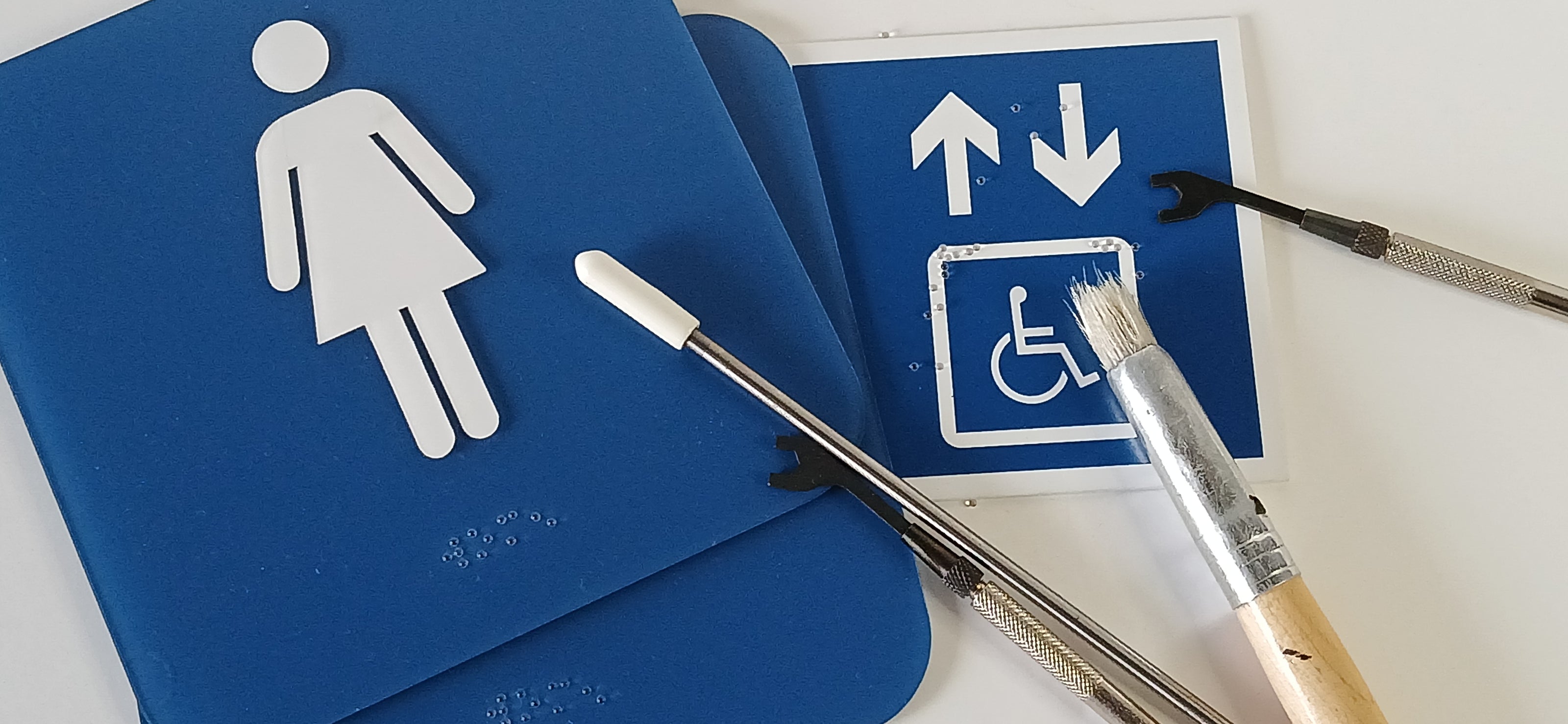 Bathroom signs with braille and raised pictograms for ADA compliance and the tools used to make them