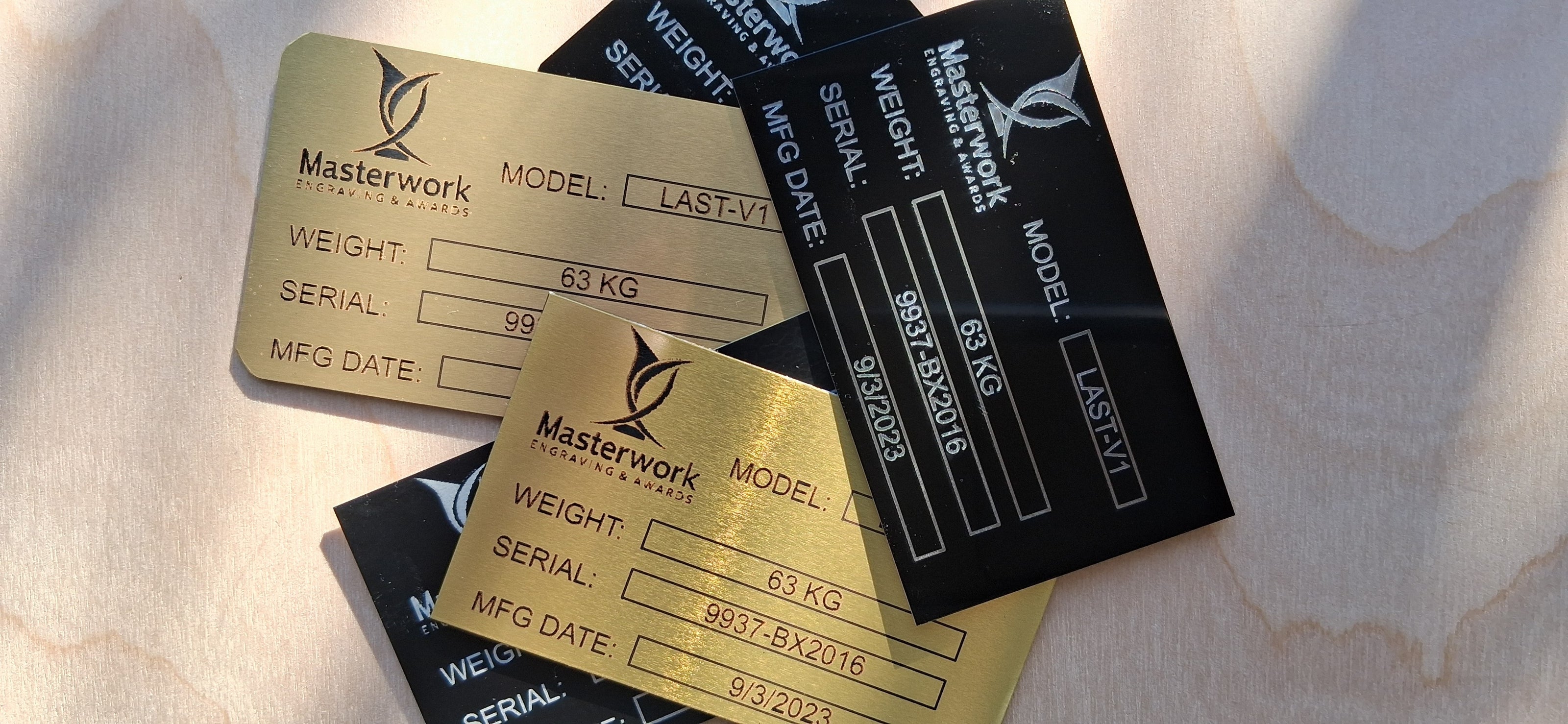 Custom engraved aluminum tags and labels with 'Masterwork Engraving and Awards' branding on a wood surface