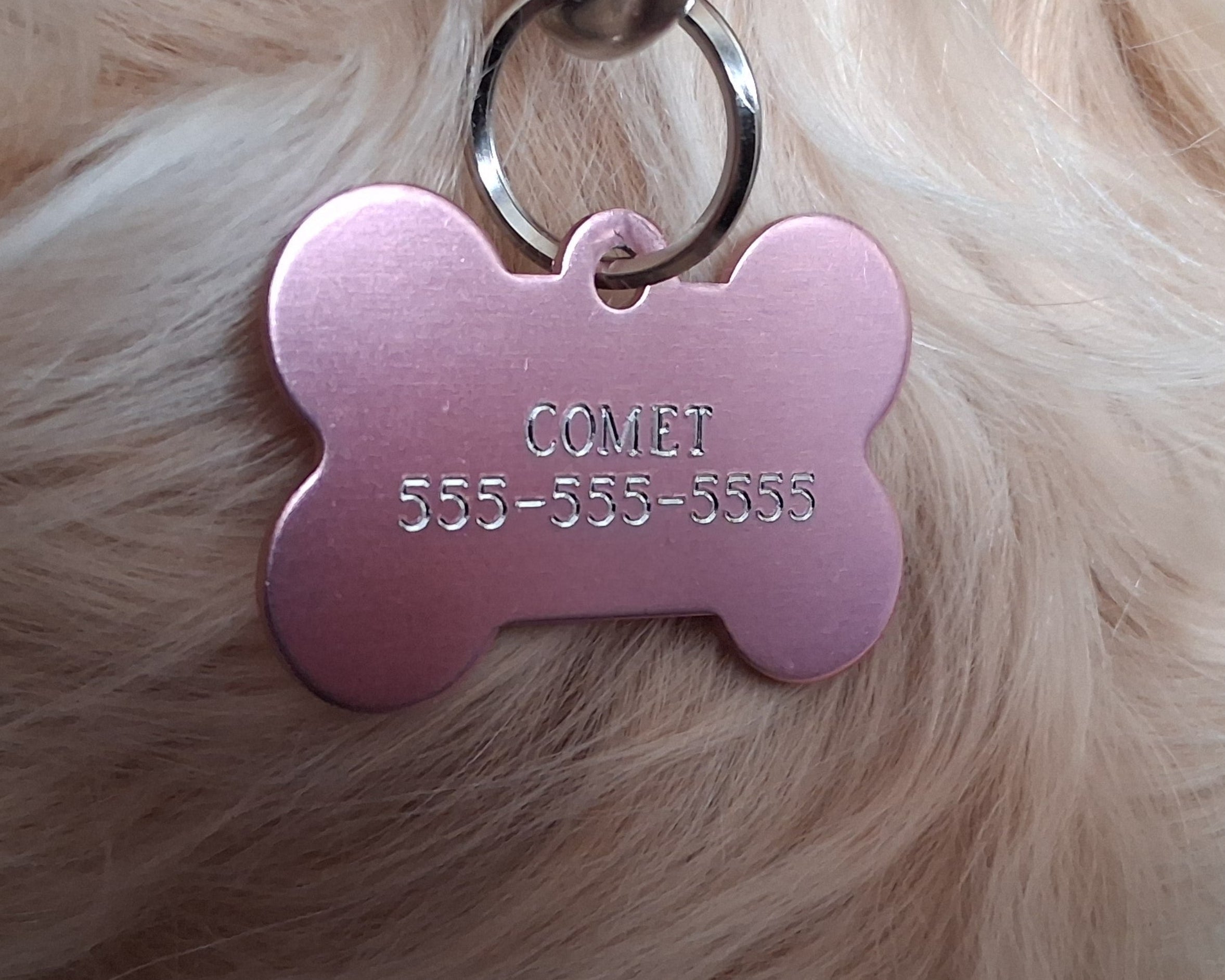 Pink bone-shaped pet tag with diamond engraved name and phone number on a fur background