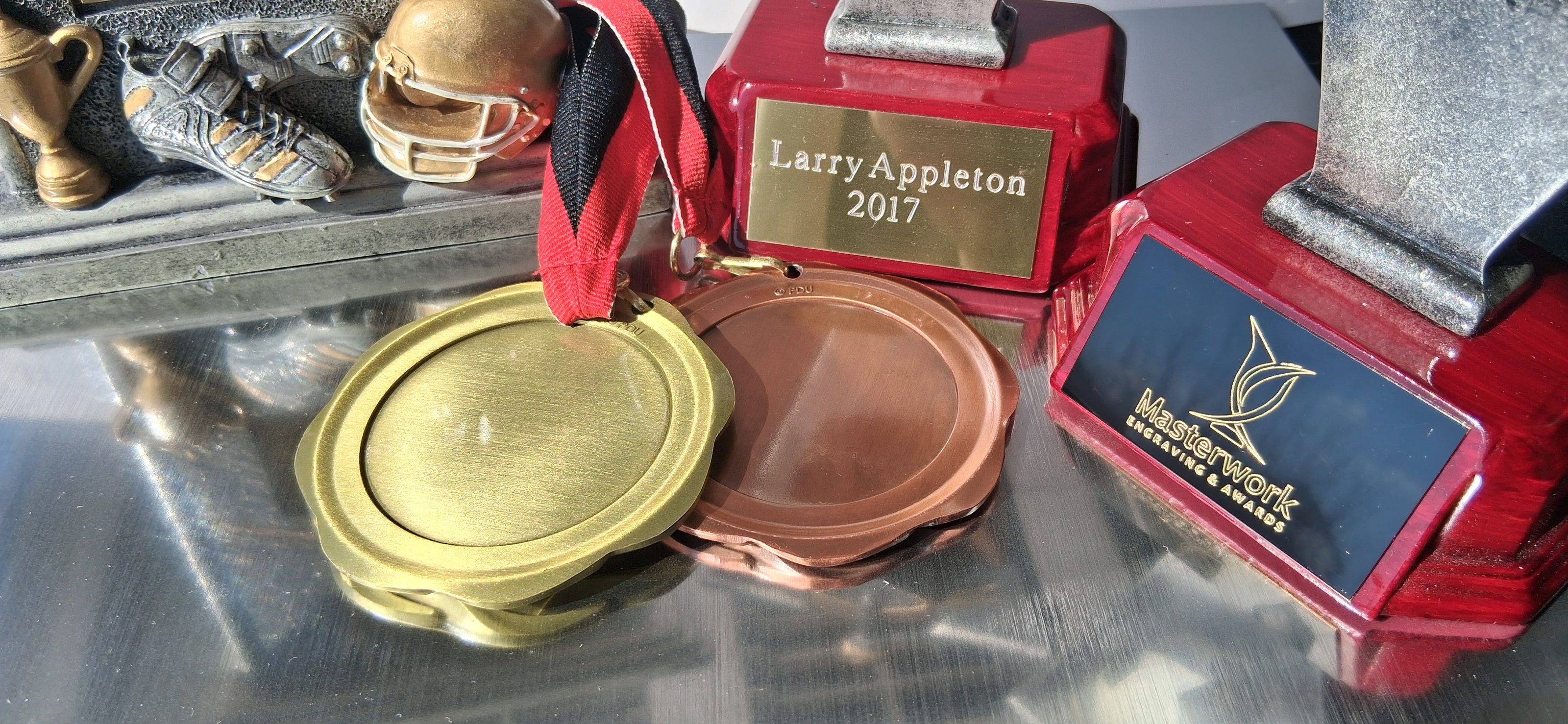 Collection of sports trophies including gold, silver, and bronze medals on a reflective surface.