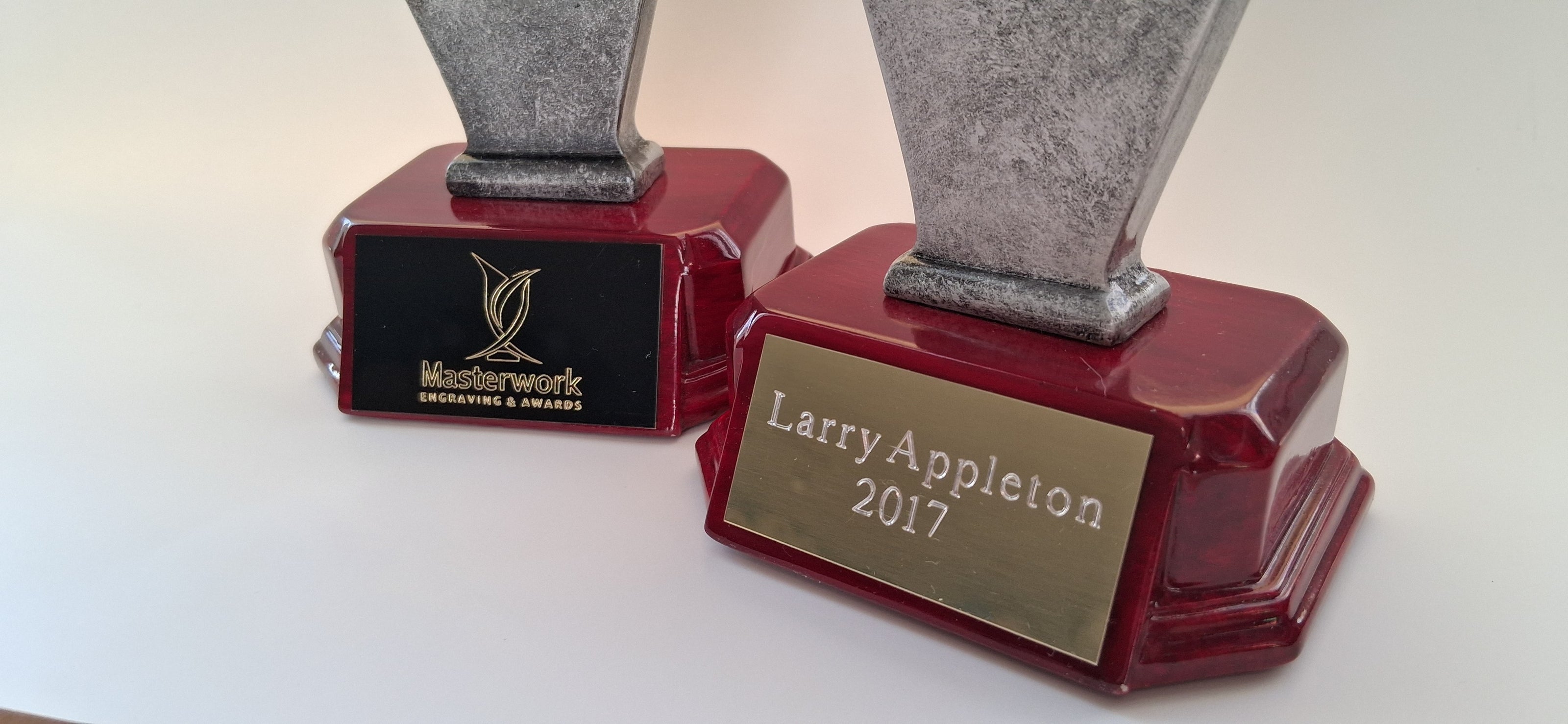 Two custom engraved awards with engraved names and logos on red bases against a white background