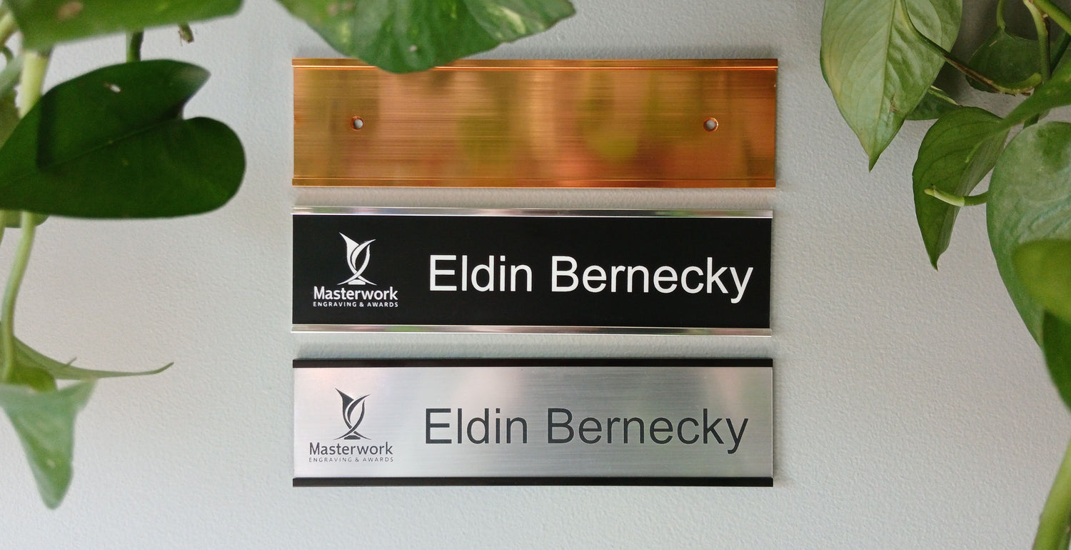 Gold, silver and black office wall nameplates with engraved plastic (lamacoid) inserts.